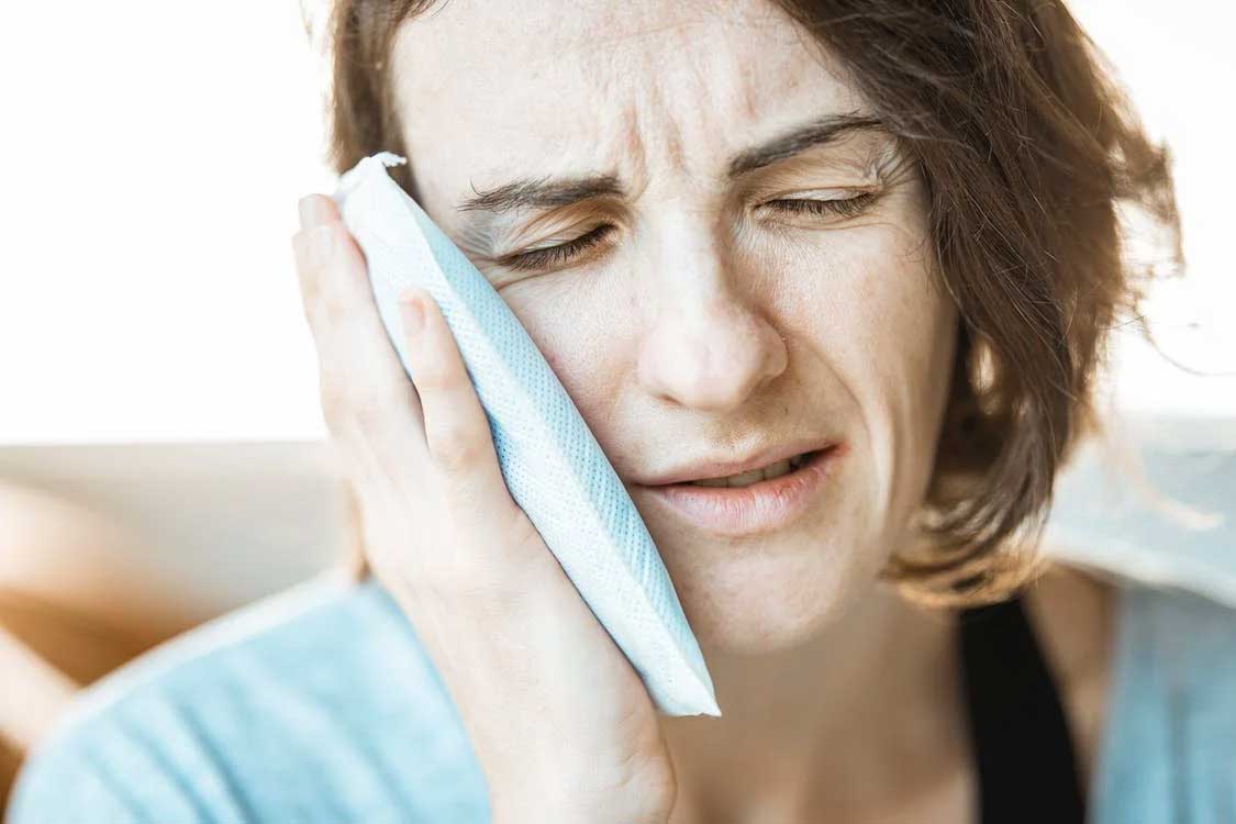 Woman with an icepack for tooth pain in need of emergency dental care in Staten Island