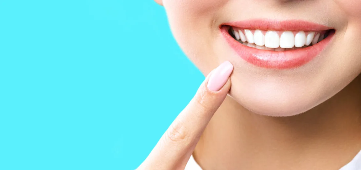 closeup of a female pointing to her new dental veneers against a light blue backdrop