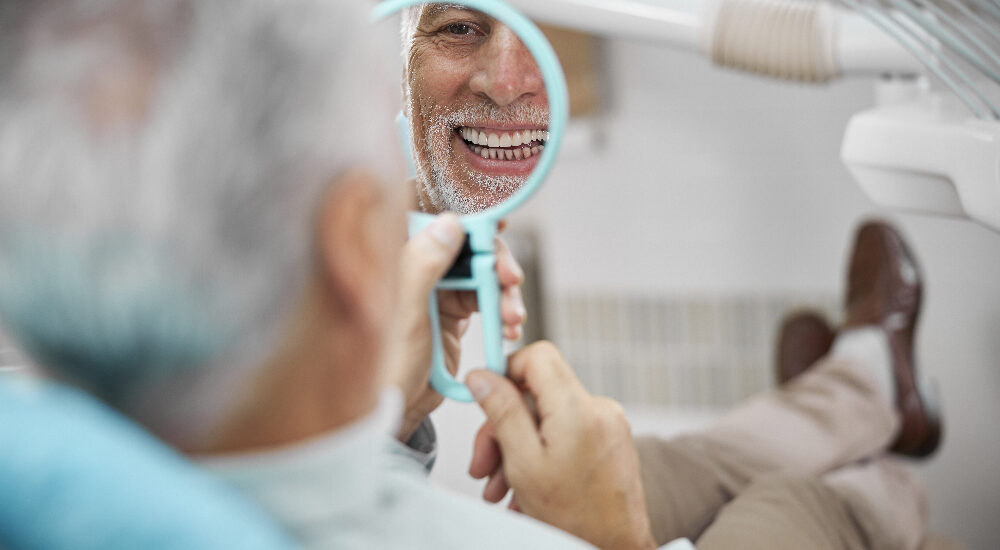 Aged patient sitting in a dental chair while looking at himself in the mirror, new dental implants