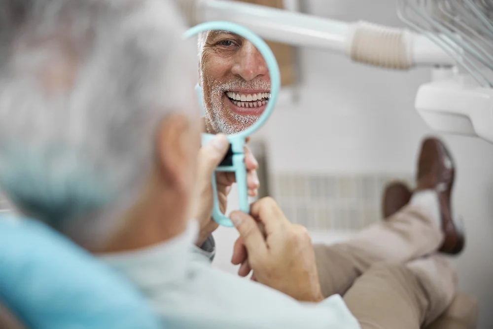Aged patient sitting in a dental chair while looking at himself in the mirror, new dental implants